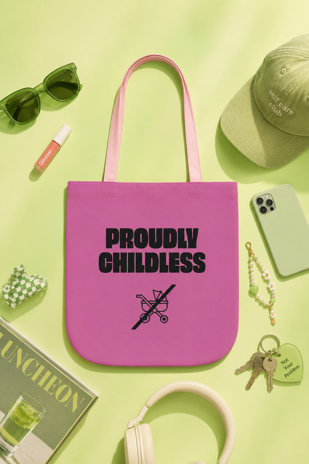 Pink Proudly Childless tote bag styled in a lime-green editorial flat lay with lifestyle accessories