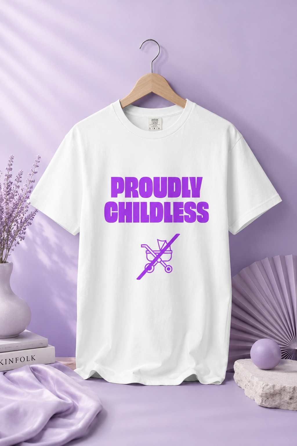 White Proudly Childless graphic T-shirt displayed on a hanger against a pastel lavender background