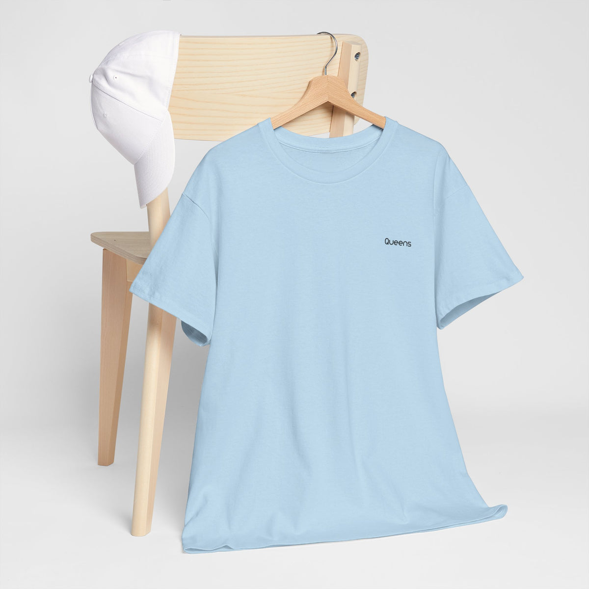 Light blue Queens crewneck T-shirt on a wooden hanger with small black Queens lettering on the left chest.