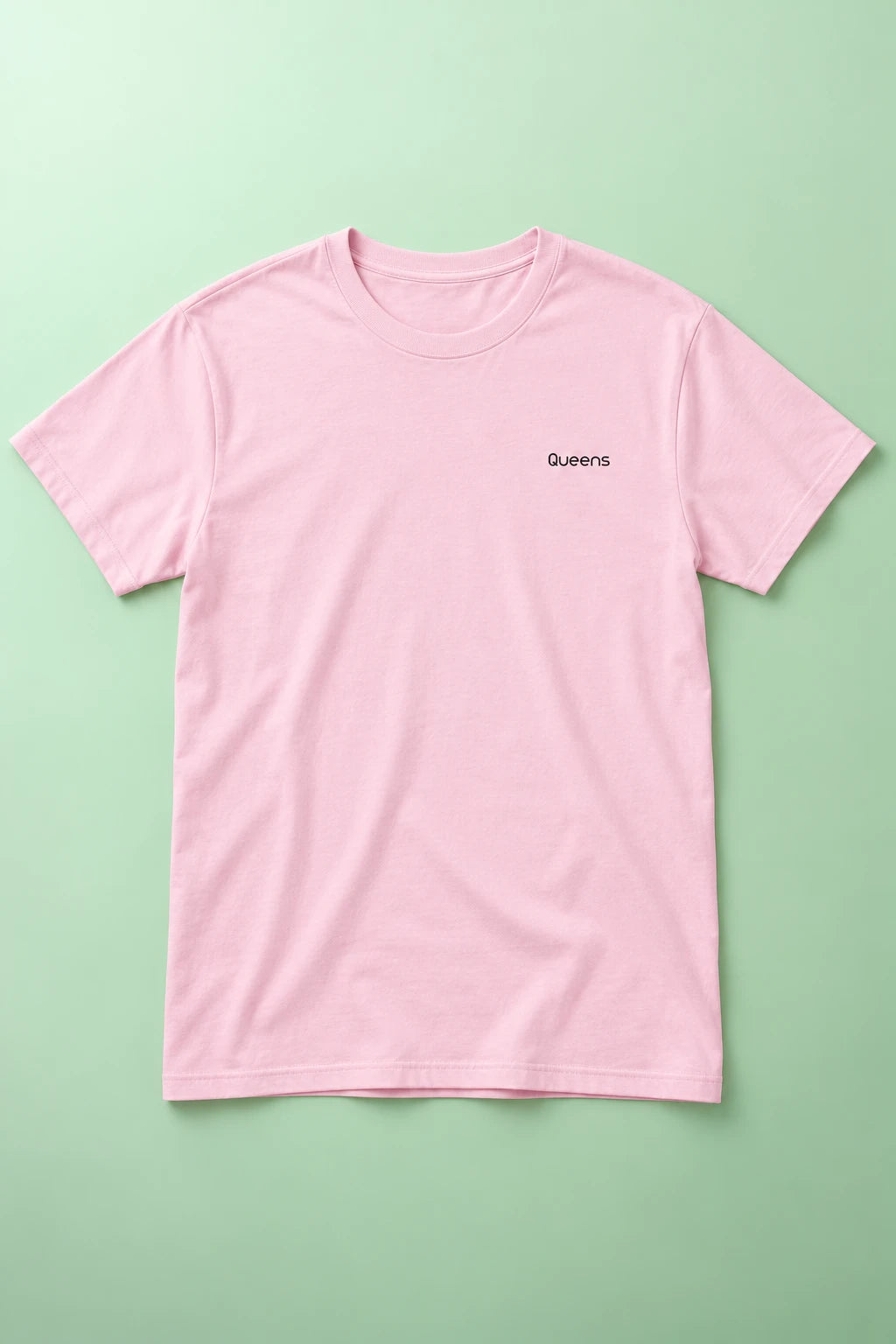 Pink Queens T-shirt laid flat on a soft mint-green gradient background with the chest lettering visible.