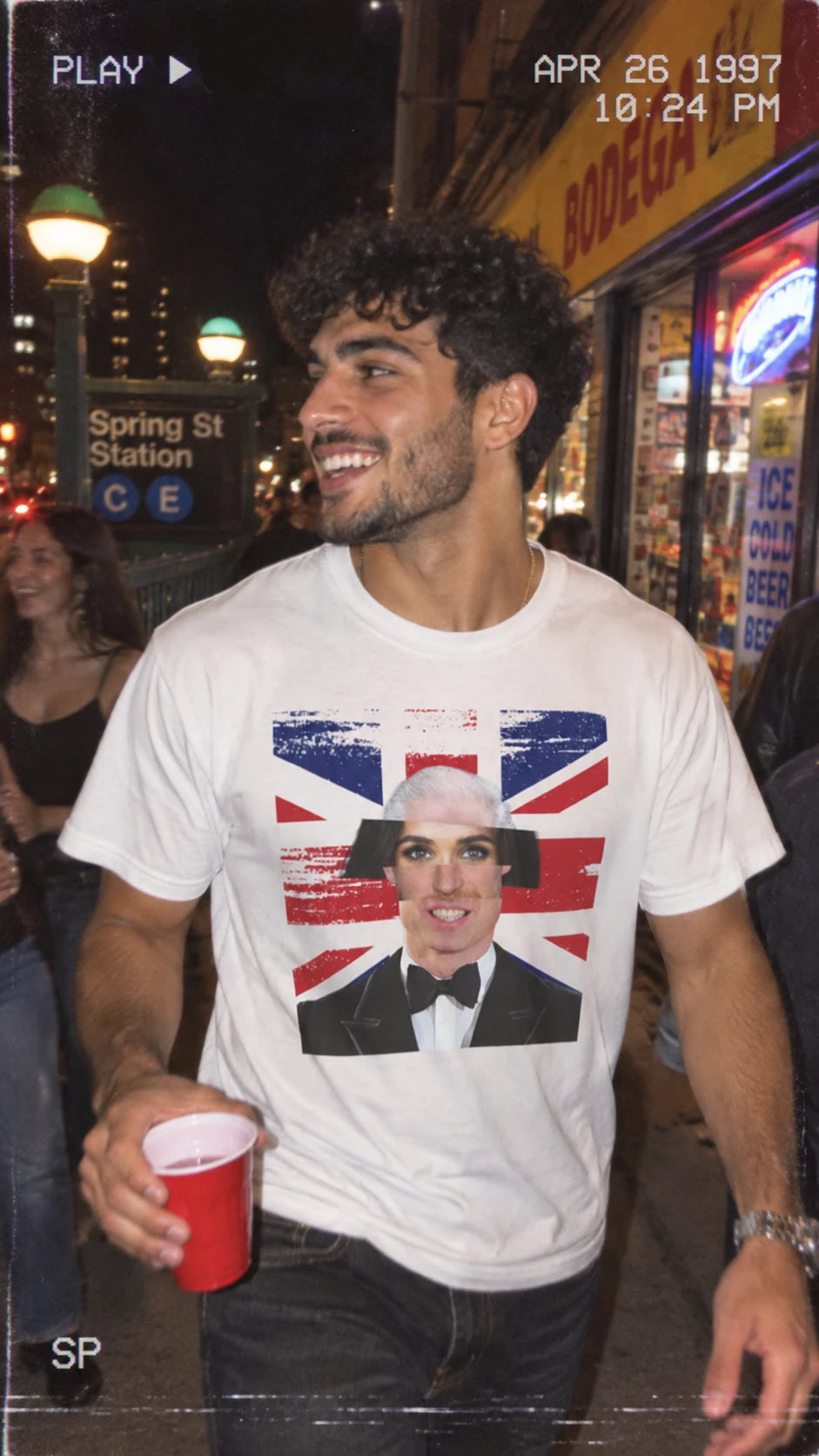 Man wearing the white Tantrum Media Royal Frankenstein T-Shirt with a royal face collage and Union Jack graphic on a New York street at night.