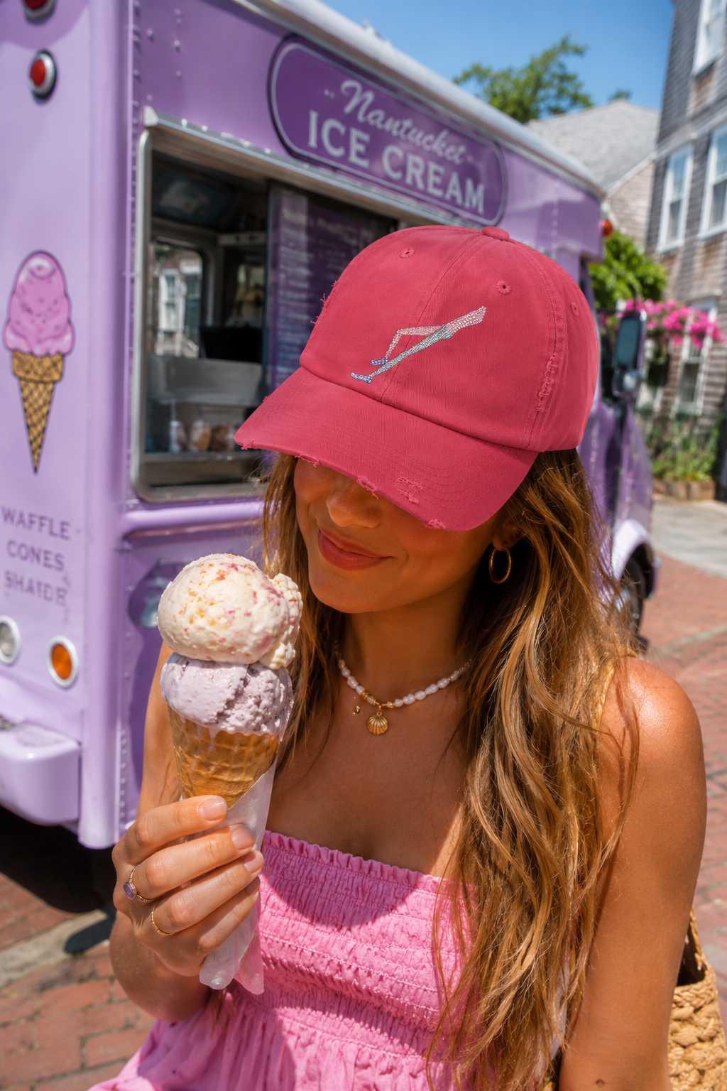 Gen Z woman wearing Shapes in Shapes red distressed baseball cap while eating ice cream beside a pastel purple ice cream truck in Nantucket.