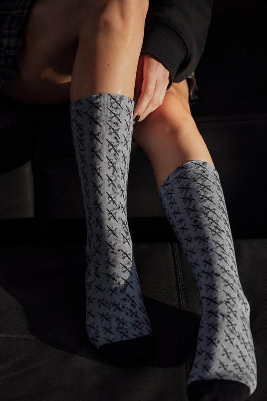 Person wearing black crew socks with repeating white scissors pattern, soft unisex statement socks by Tantrum Media.