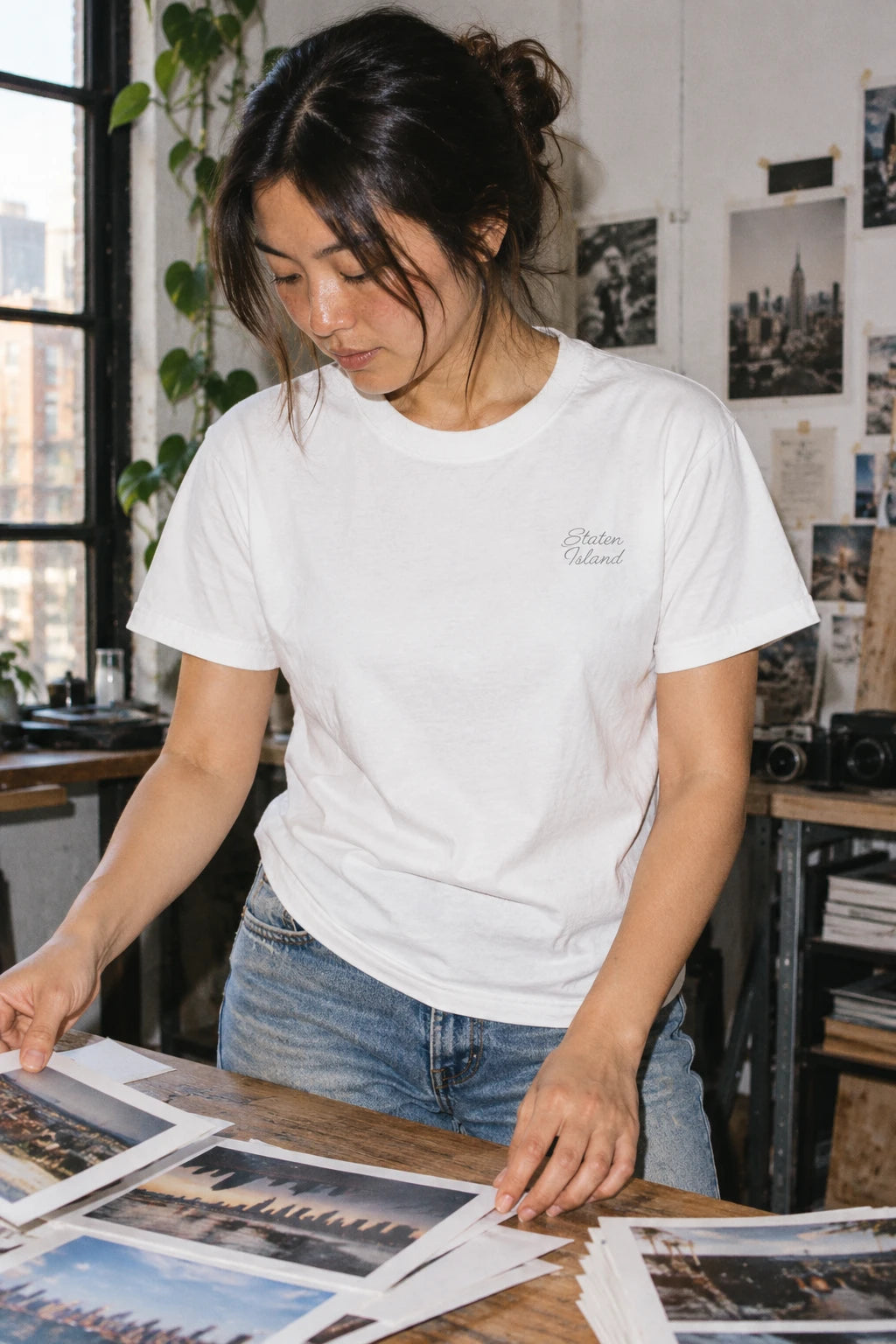Woman wearing a white Staten Island T-shirt while sorting photographic prints at a studio worktable.