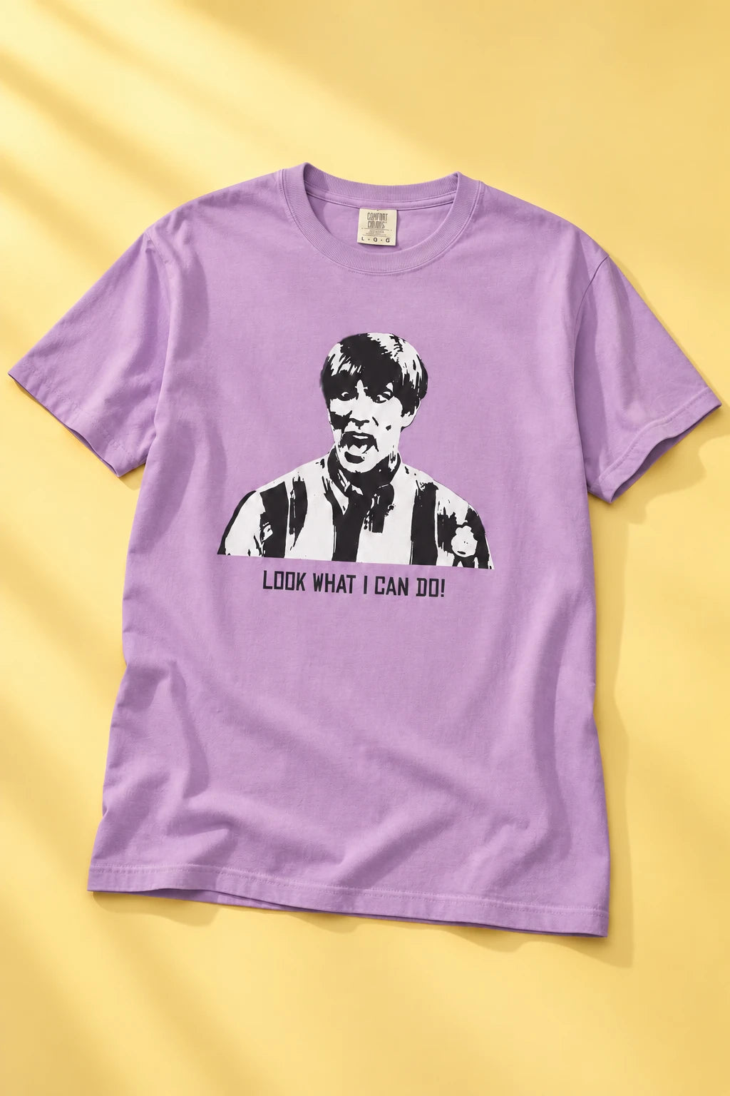 Lavender Tantrum Media Stuart MadTV Unisex T-Shirt laid flat on yellow, showing the portrait and “Look What I Can Do!” graphic.
