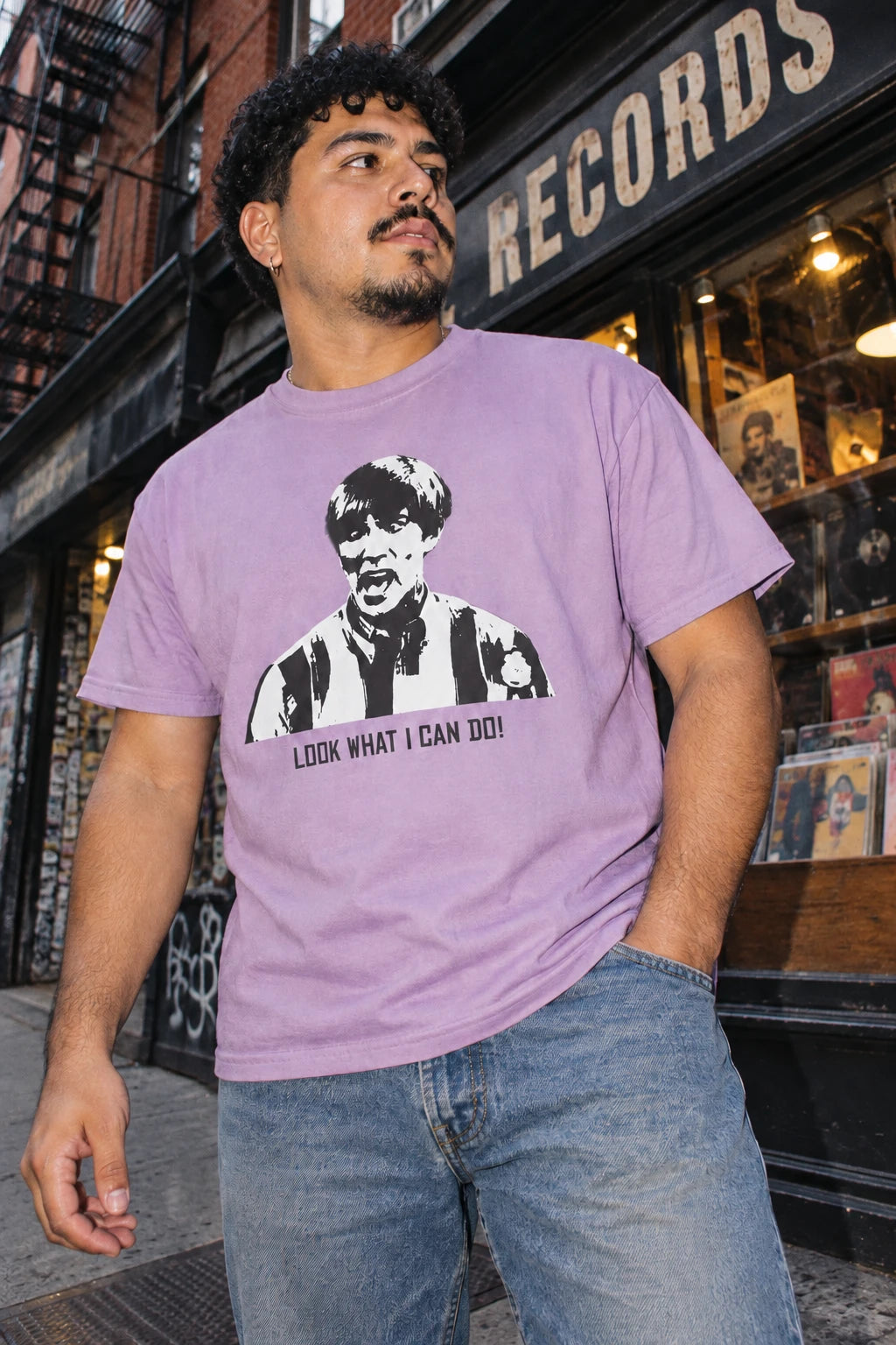 Man wearing the lavender Tantrum Media Stuart MadTV Unisex T-Shirt with jeans outside a record store.