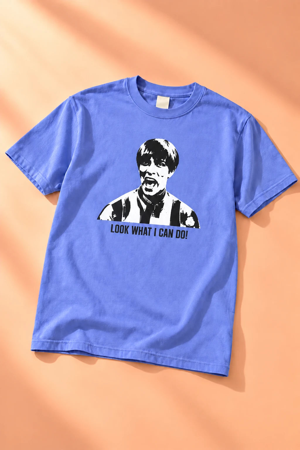 Periwinkle blue Tantrum Media Stuart MadTV Unisex T-Shirt laid flat on peach with the front graphic clearly visible.