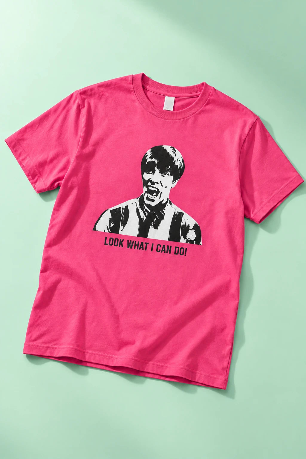 Bright pink Tantrum Media Stuart MadTV Unisex T-Shirt laid flat on mint with the “Look What I Can Do!” graphic visible.