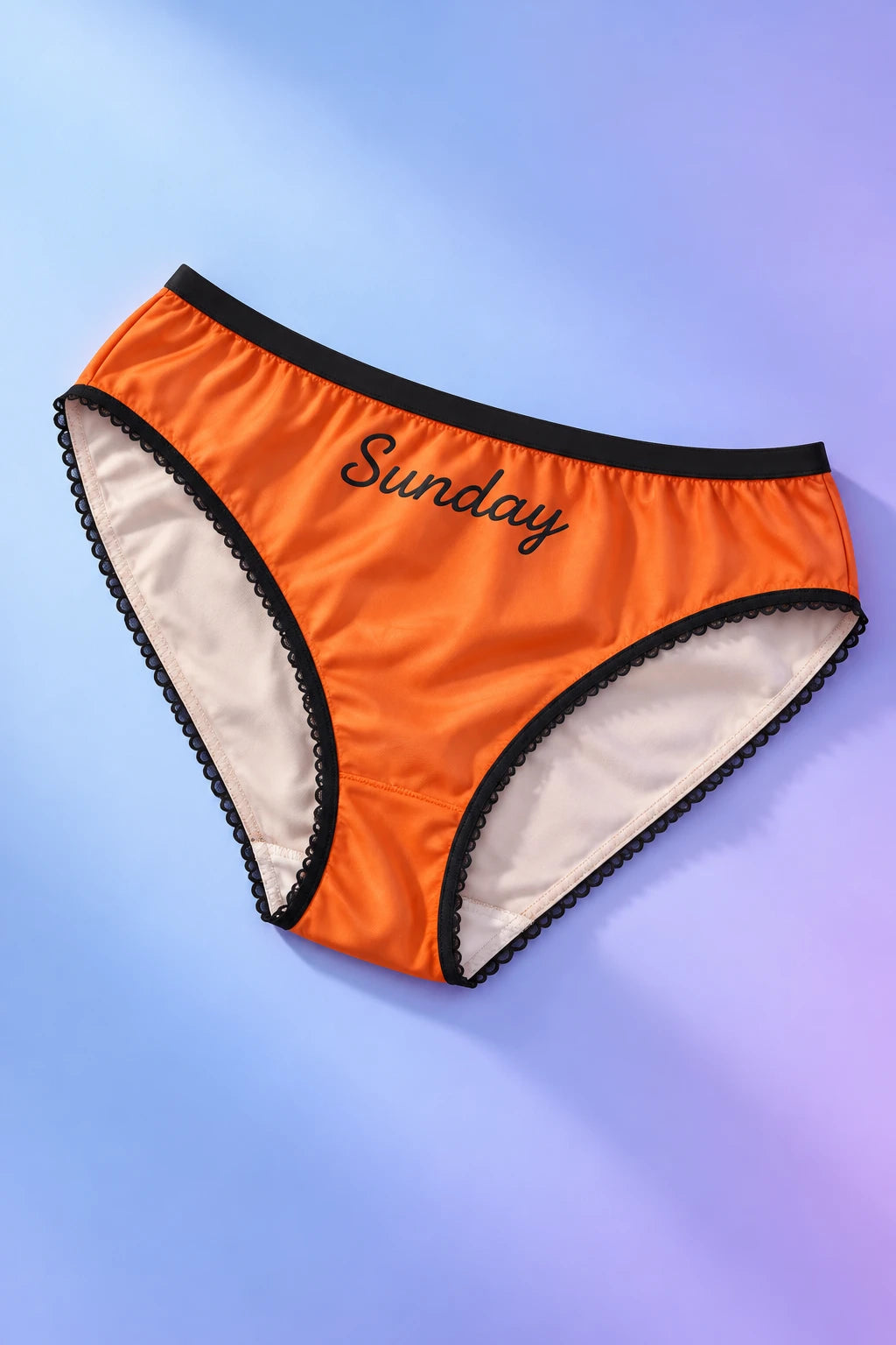 Tantrum Media Sunday Panty in orange with black Sunday script and scalloped trim, laid flat on a blue and lavender gradient background.