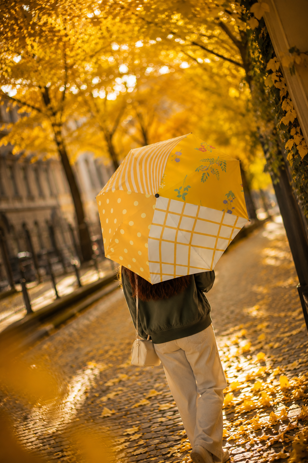 Young woman carrying Sunny Side Patchwork umbrella beneath golden ginkgo trees in a cinematic NYC autumn scene