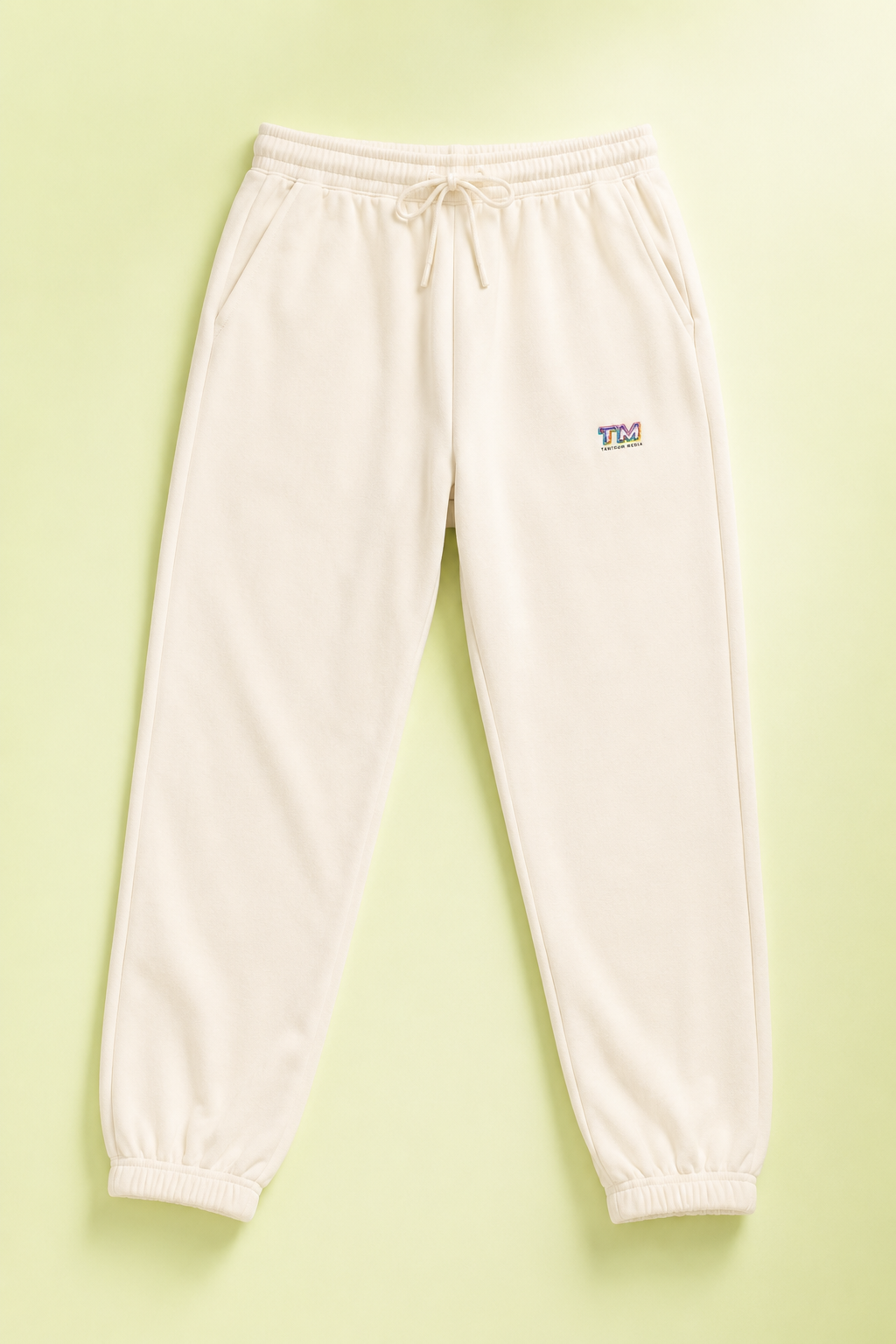Ivory Tantrum Media sweatpants flat lay on a soft pastel lime green background.