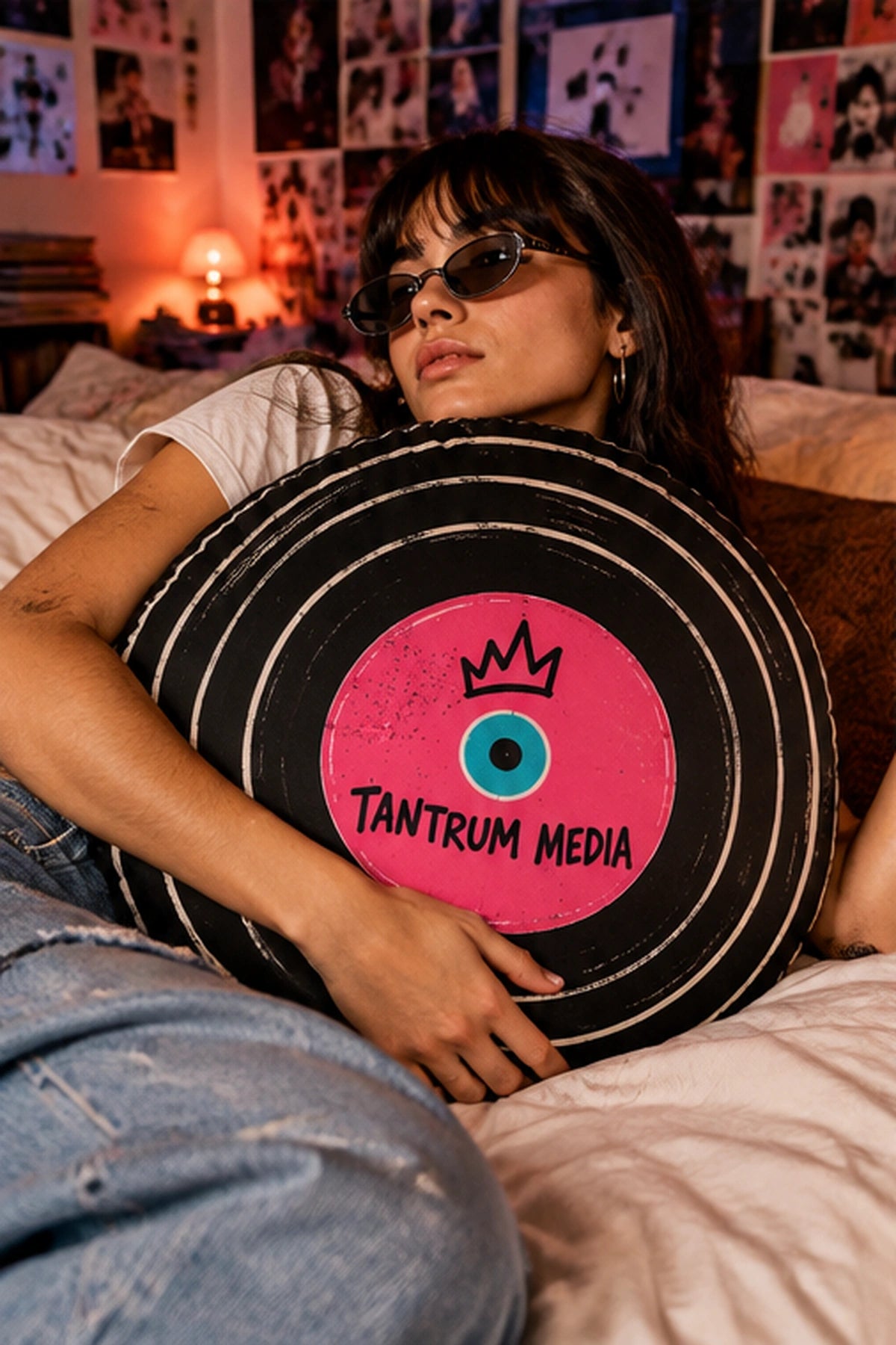 Young woman relaxing on a bed with the Tantrum Media LP Record Pillow, a round black vinyl record cushion with a hot-pink label and retro music design.