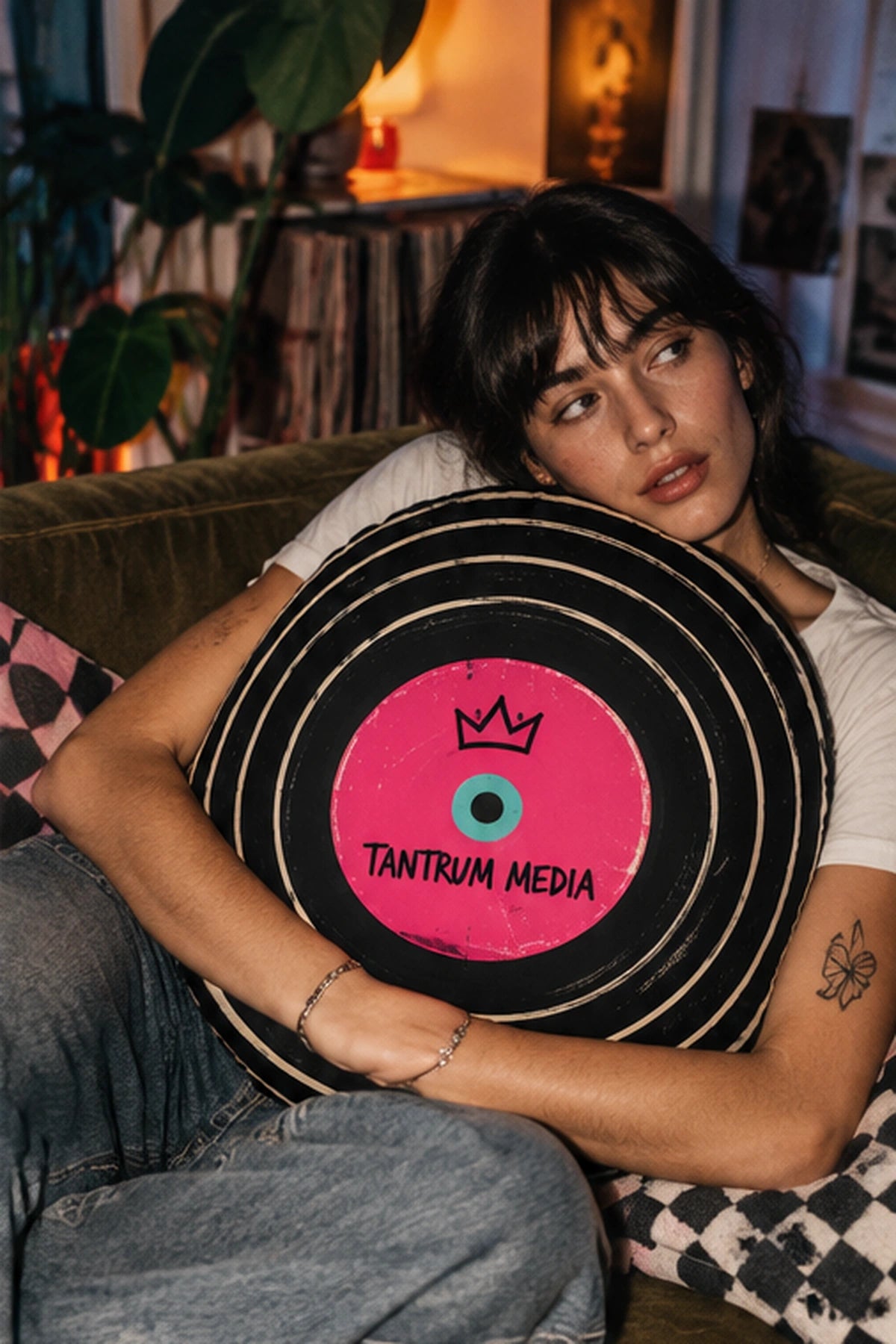 Young woman with dark hair relaxing on a sofa while holding the Tantrum Media LP Record Pillow, a round retro vinyl record cushion with a pink center label.
