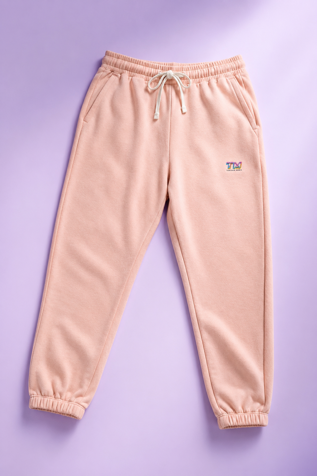 Peach Tantrum Media sweatpants flat lay on a soft pastel lavender background.