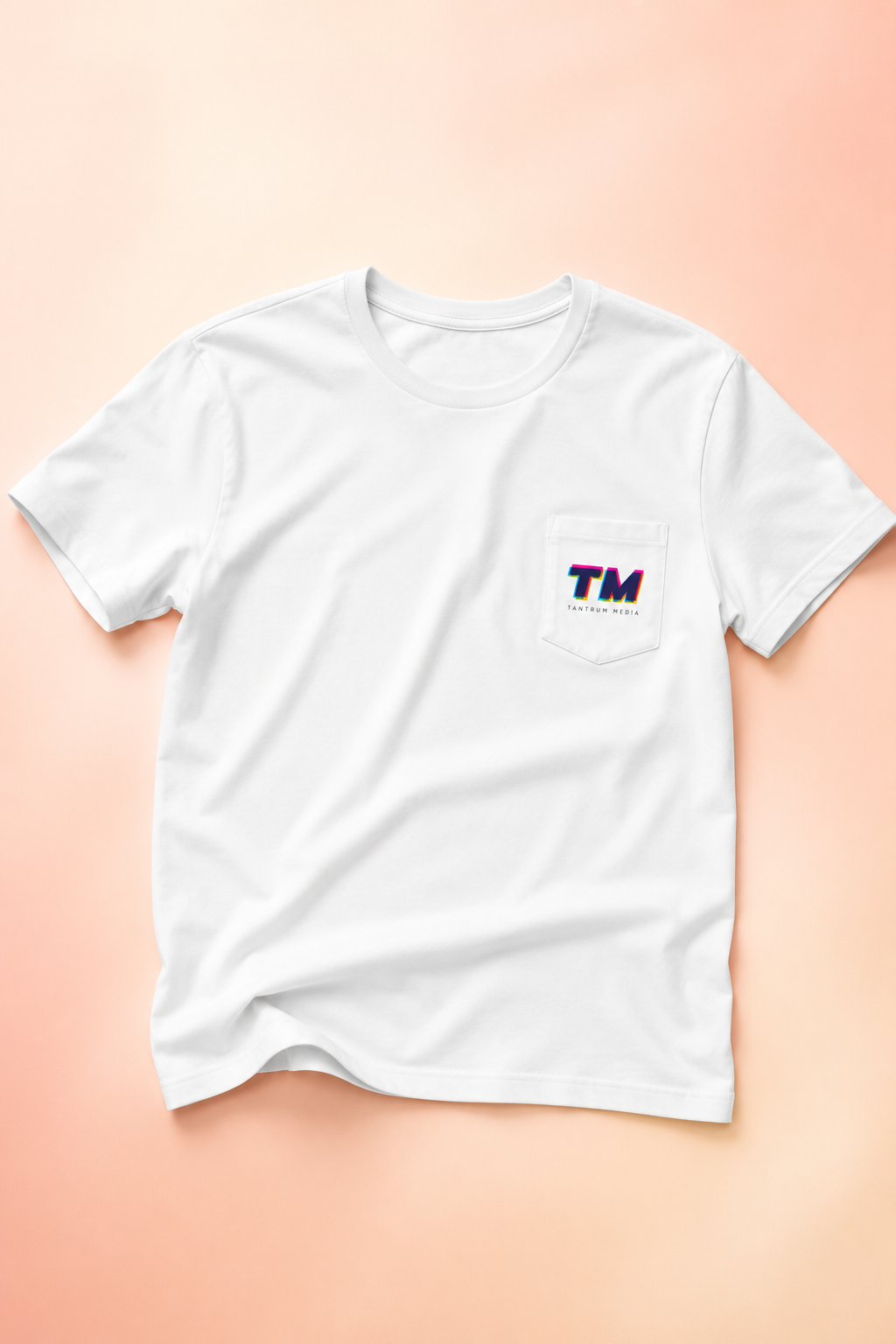 Flat lay of the Tantrum Media Premium Pocket T-Shirt on a soft pastel peach gradient background.