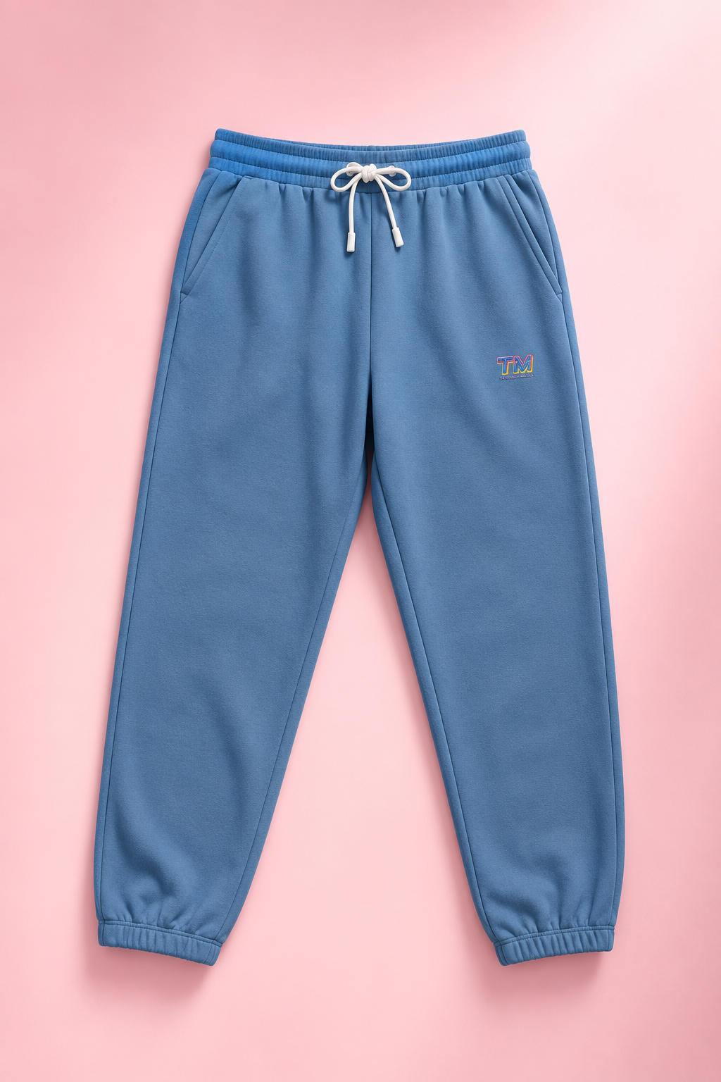 Sky blue Tantrum Media sweatpants flat lay on a soft pastel pink background.