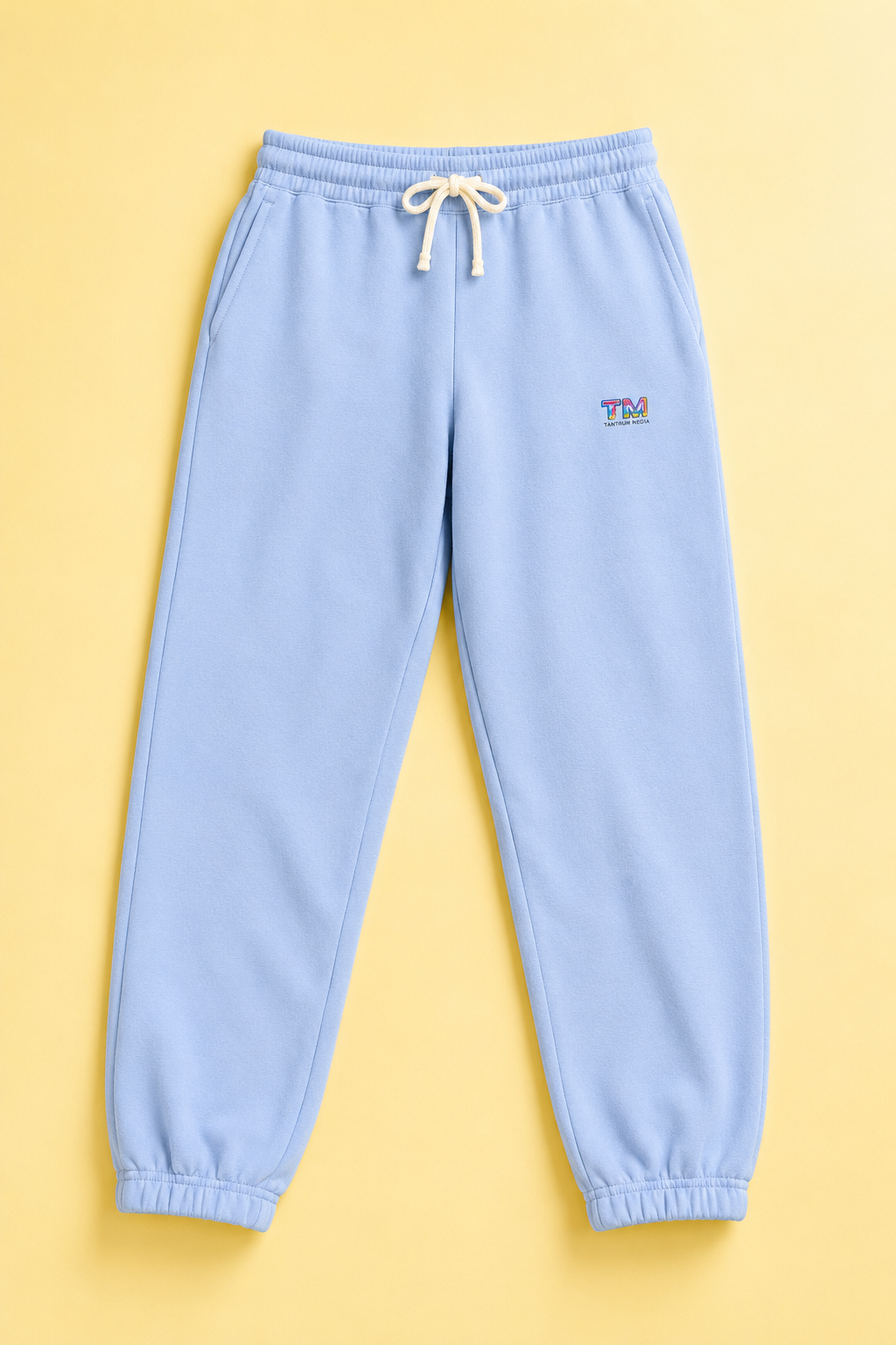 Sky blue Tantrum Media sweatpants flat lay on a soft pastel yellow background.