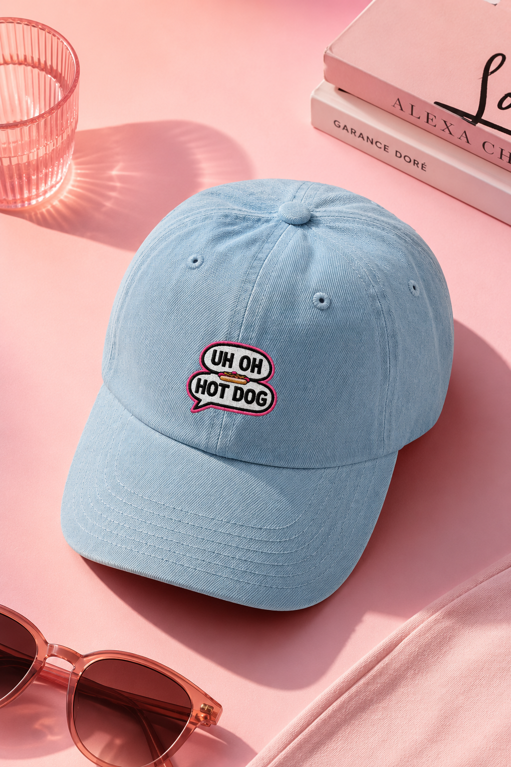 Light blue UH OH HOT DOG embroidered hat flat lay on soft pink background