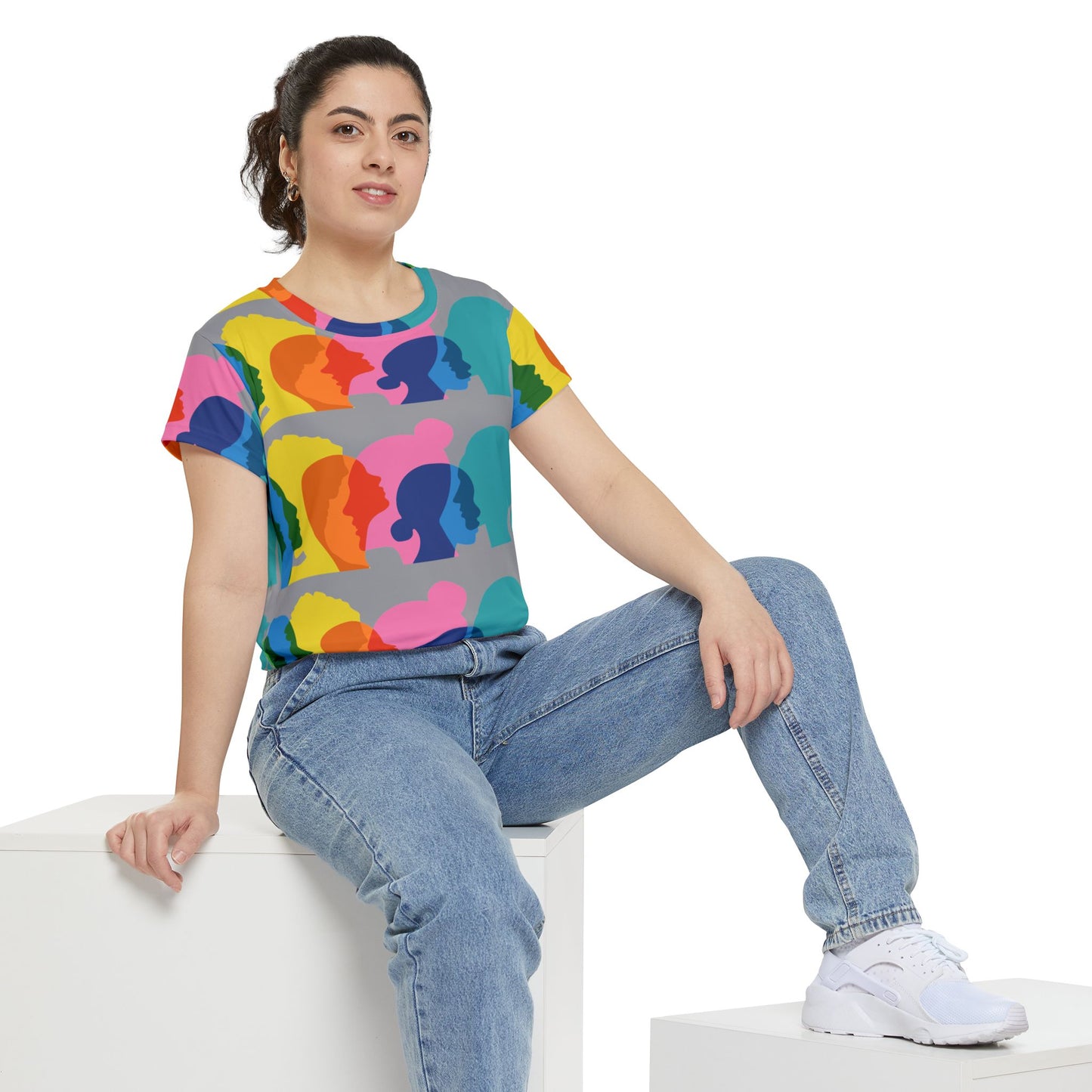 Person wearing a colorful graphic t-shirt and blue jeans sitting on a white surface.