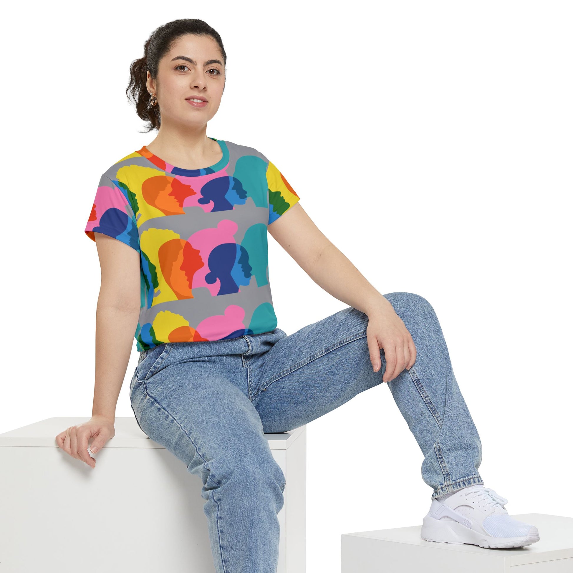 Person wearing a colorful graphic t-shirt and blue jeans sitting on a white surface.