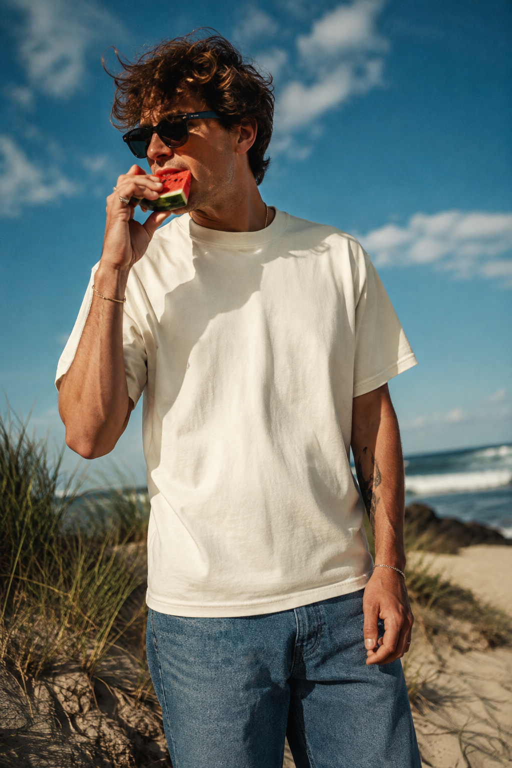 Millennial man wearing white heavyweight t-shirt while eating watermelon at the beach