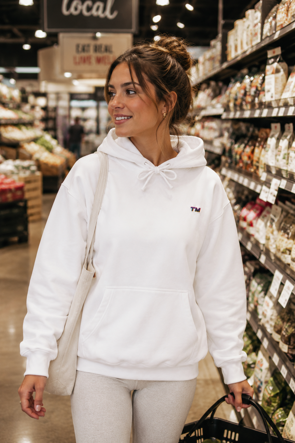 Female millennial grocery shopping in a suburban supermarket wearing the Tantrum Media EcoSmart white hoodie.
