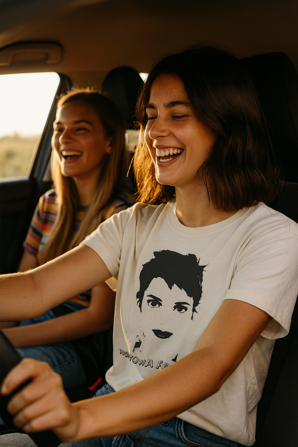Winona Forever T-Shirt white graphic tee worn by two friends laughing while driving in a car