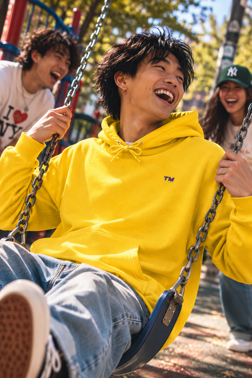 Asian Gen Z enjoying swings at a playground wearing the Tantrum Media EcoSmart yellow hoodie.