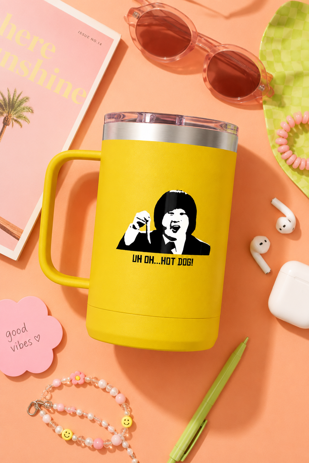 Yellow Uh Oh Hot Dog MADtv travel mug in a colorful flat lay with sunglasses and accessories