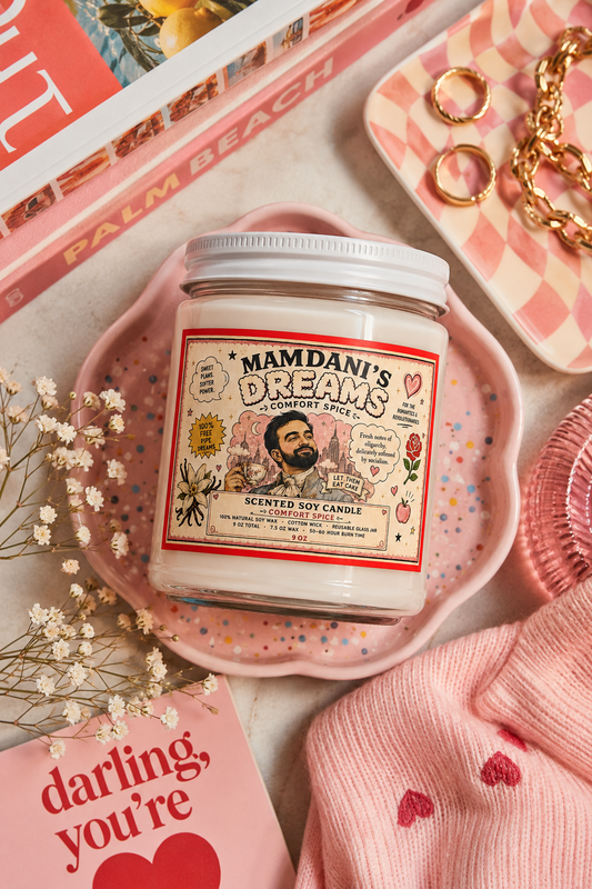 Zohran Mamdani’s Dreams Comfort Spice candle styled in a colorful pink editorial flat lay